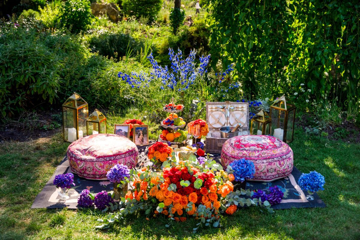 A luxury Parisian picnic in a verdant garden (Parc Monceau) with Champagne, cushions, and vibrant orange flowers.
