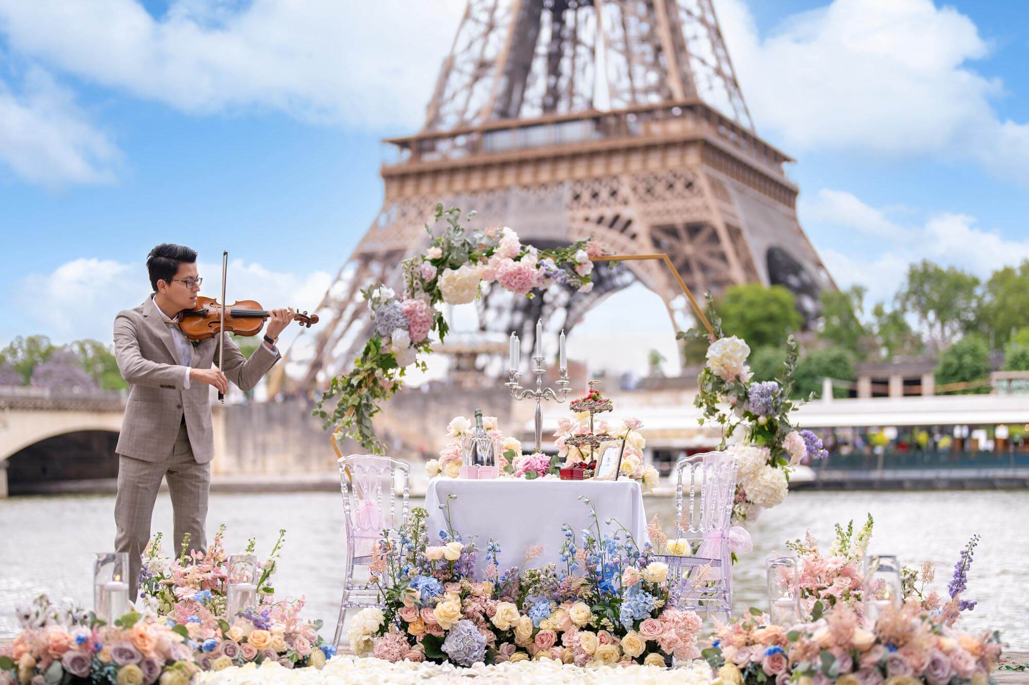 Elegant garden proposal setup surrounded by fresh flowers, a magnificent table with Ladurée macarons, pastries, a chandelier, and Ruinart champagne.